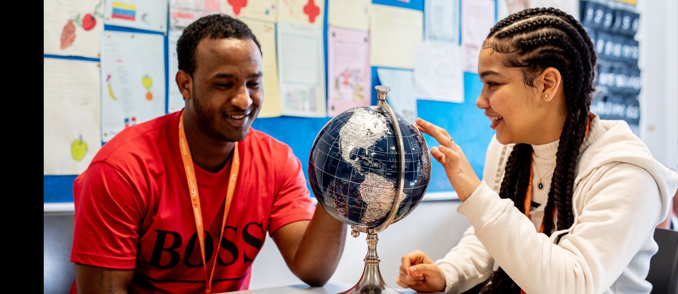 Two Lambeth College ESOL students, a boy and girl, examining a globe together, sharing a moment of exploration and learning.