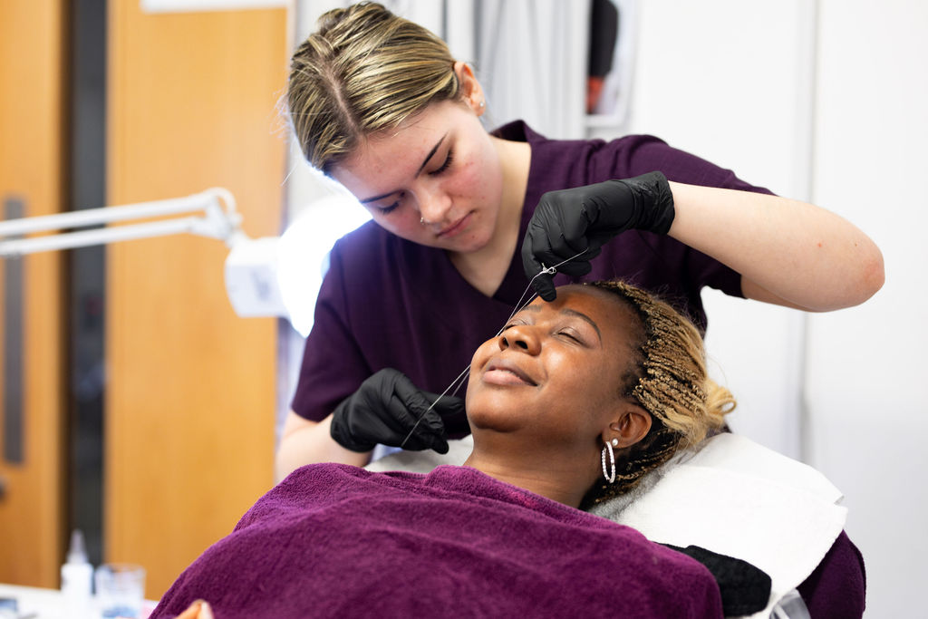 A beauty student threading a clients eyebrows